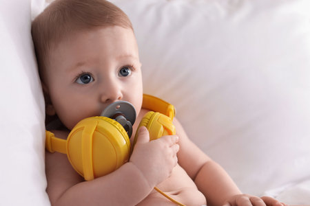 Cute little baby with headphones and pacifier on bed at homeの写真素材