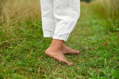 Little child standing barefoot on green grass outdoors, closeup. Enjoying nature