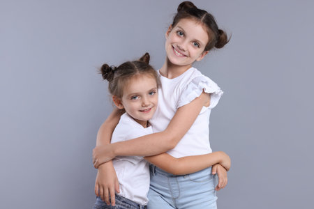 Portrait of cute little sisters on grey backgroundの写真素材