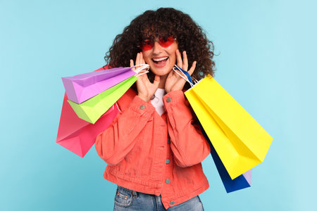 Happy woman with colorful shopping bags on light blue backgroundの写真素材