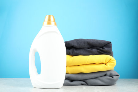 Laundry detergent in bottle and clothes on gray marble table against light blue backgroundの写真素材