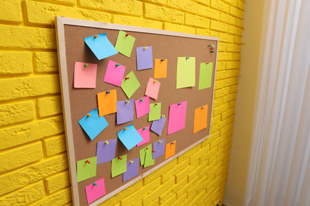 Corkboard filled with colorful notes and pins on yellow brick wall indoors
