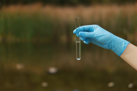 Examination of water quality. Researcher holding test tube with sample outdoors, closeup. Space for...
