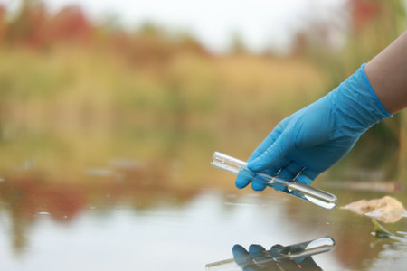 Examination of water quality. Researcher taking water sample from lake outdoors, closeup. Space for...