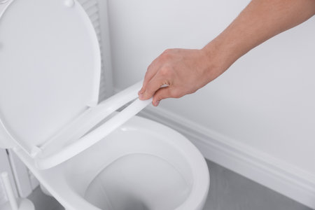 Man closing toilet seat in bathroom, closeup