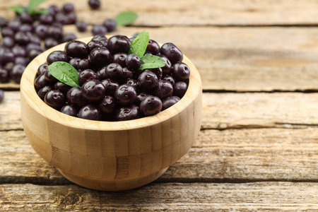 Ripe acai berries and leaves in bowl on wooden table, closeup. Space for textの写真素材
