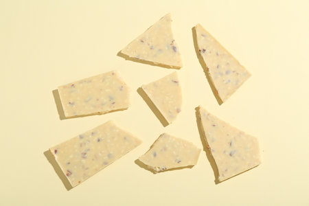 Pieces of tasty white chocolate on beige background, top view
