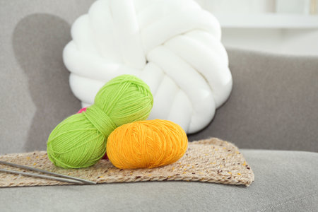 Skeins of soft yarn and knitting needles on sofa indoors