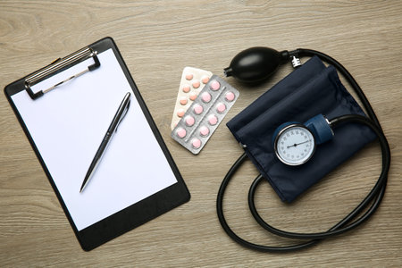 Blood pressure measuring device, pills and clipboard on wooden table, top viewの写真素材
