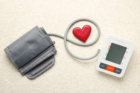 Blood pressure measuring device and heart figure on light textured background, top view
