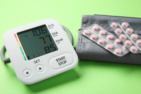 Blood pressure measuring device and pills on green background, closeup
