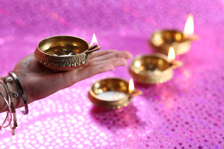 Diwali celebration. Woman holding lit diya lamp on pink background, closeupの写真素材