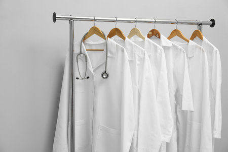 Different medical workers' uniforms and stethoscope on clothing rack against gray backgroundの写真素材