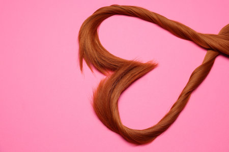 Red hair strands in the shape of heart on pink background, top view. Space for textの写真素材