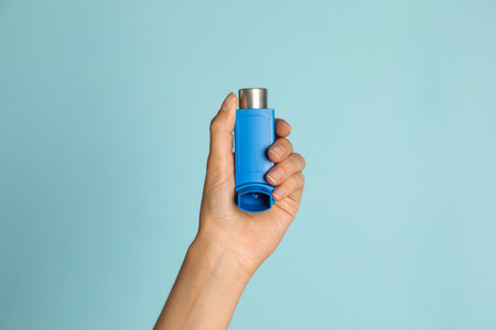 Woman holding asthma inhaler on light blue background, closeupの写真素材