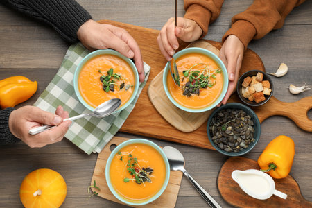 Woman and man eating delicious pumpkin soup at wooden table, top viewの写真素材