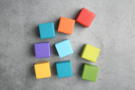 Many wooden colorful cubes on gray textured background, top view