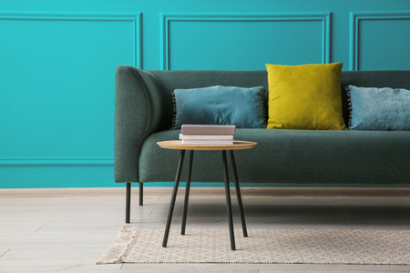 Comfortable sofa and table near teal color wall in room