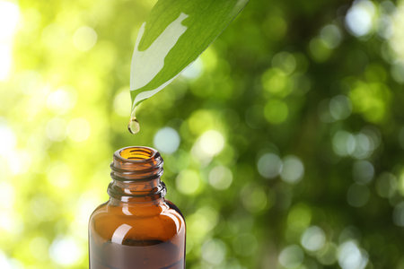 Essential oil dripping from green leaf into bottle on blurred background, closeup. Space for textの写真素材