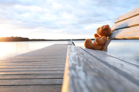 Lonely teddy bear on bench near riverの写真素材