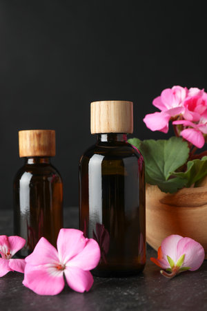 Bottles of geranium essential oil and beautiful flowers on black table, closeupの写真素材