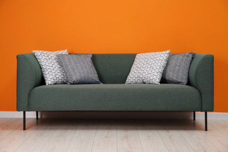Stylish sofa with pillows near orange wall indoorsの写真素材
