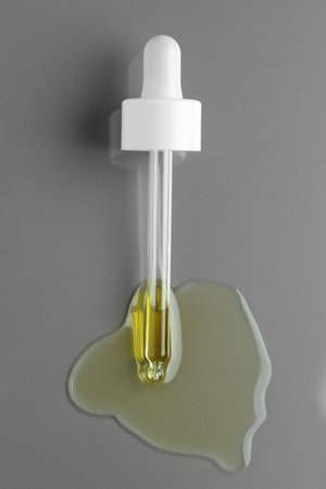 Dripping essential oil from pipette on gray background, top view