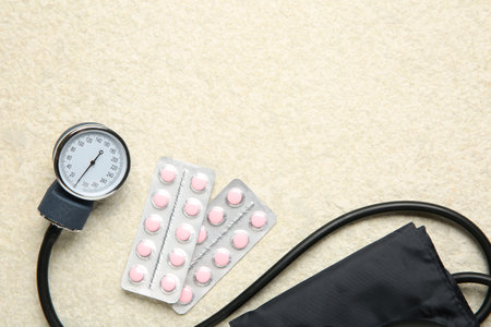 Blood pressure measuring device and pills on light textured background, top view. Space for text