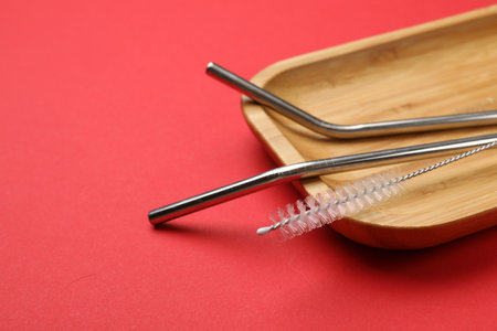 Metal drinking straws and cleaning brush on red background, closeup. Space for text