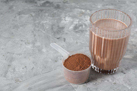 Delicious protein shake in glass and scoop with powder on gray table, closeup. Space for text