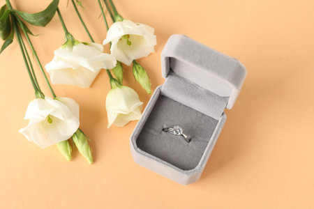 Beautiful ring with gemstone in box and flowers on beige background, flat lay