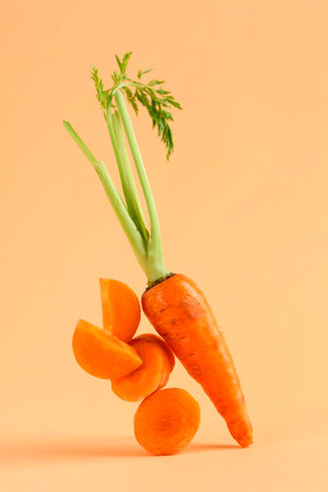 Whole and cut fresh carrots on pale orange background