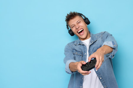 Happy young man playing video games with controller on light blue background, space for text