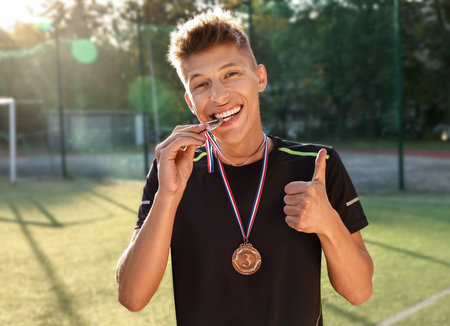 Happy winner with different medals showing thumbs up at stadium on sunny dayの写真素材