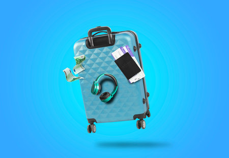 Suitcase, headphones, euro bills and passport with tickets in air on light blue backgroundの写真素材