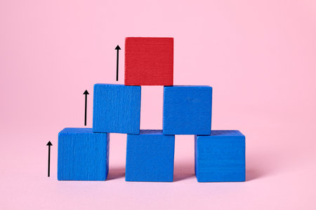 Pyramid made of wooden blocks on pink background. Cubes and arrows showing the way to red one. Steps...