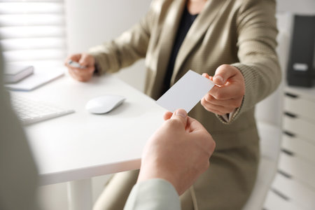Woman giving business card to man at table in office, closeup. Mockup for designの写真素材
