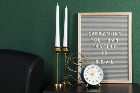 Letter board with phrase Everything You Can Imagine Is Real, alarm clock, candles and decor element...