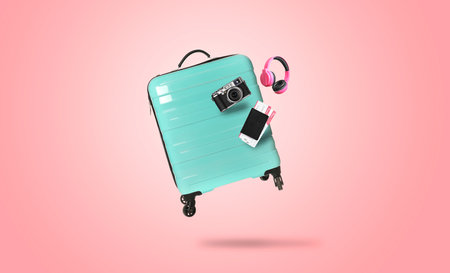 Turquoise suitcase, camera, headphones and passport with tickets in air on pink backgroundの写真素材