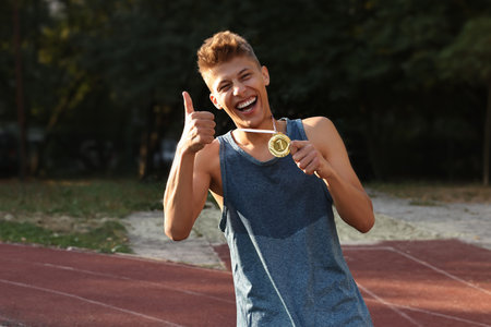 Happy winner with golden medal showing thumbs up at stadiumの写真素材