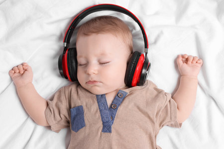 Cute little baby with headphones sleeping on bed, top viewの写真素材