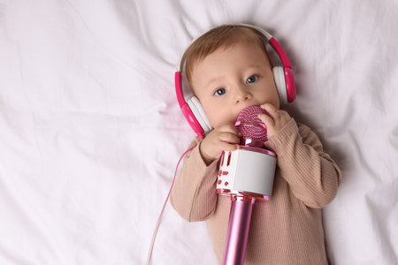 Cute little baby with headphones and microphone lying on bed, top viewの写真素材