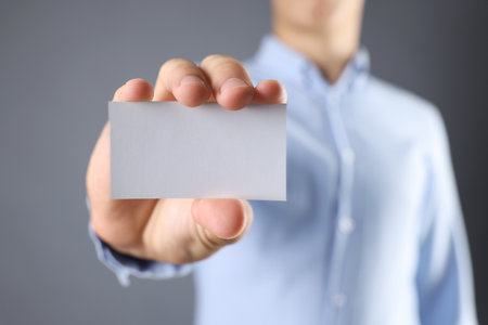 Man holding blank business card on gray background, closeup. Mockup for designの写真素材