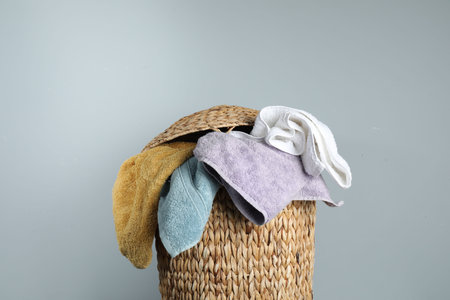 Wicker basket full of laundry on gray background