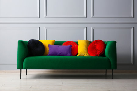 Stylish green sofa with different cushions near gray wall