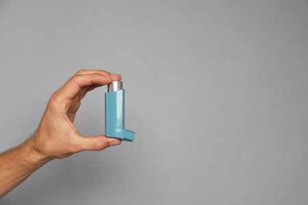 Man holding asthma inhaler on gray background, closeup. Space for textの写真素材