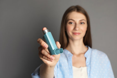Young woman using asthma inhaler on gray background, selective focusの写真素材