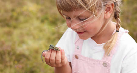 Happy little girl holding small lizard outdoors, space for textの写真素材