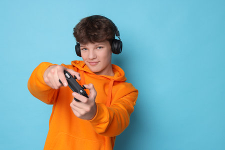 Teenage boy in headphones playing video game with controller on light blue background. Space for textの写真素材