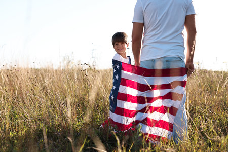 Father and son with flag of USA outdoors, back view. Space for textの写真素材